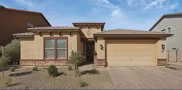 Single-story stucco home with stone trim, desert landscaping and a paver driveway